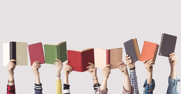 Multiple hands holding colorful books overhead