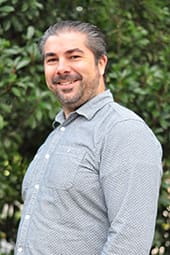 Smiling man in patterned gray shirt outdoors